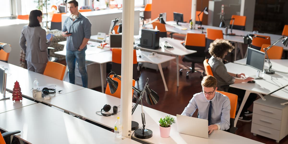 Photograph of colleagues working in a modern office space. Some are working at their desks; others are standing and conversing. 