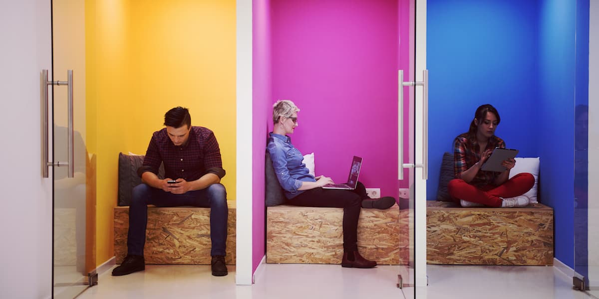 Three coworkers in small meeting rooms, working on electronic devices.
