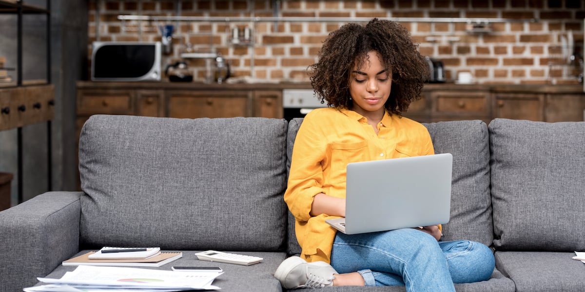 Photograph of a person using a laptop while sitting on a sofa.