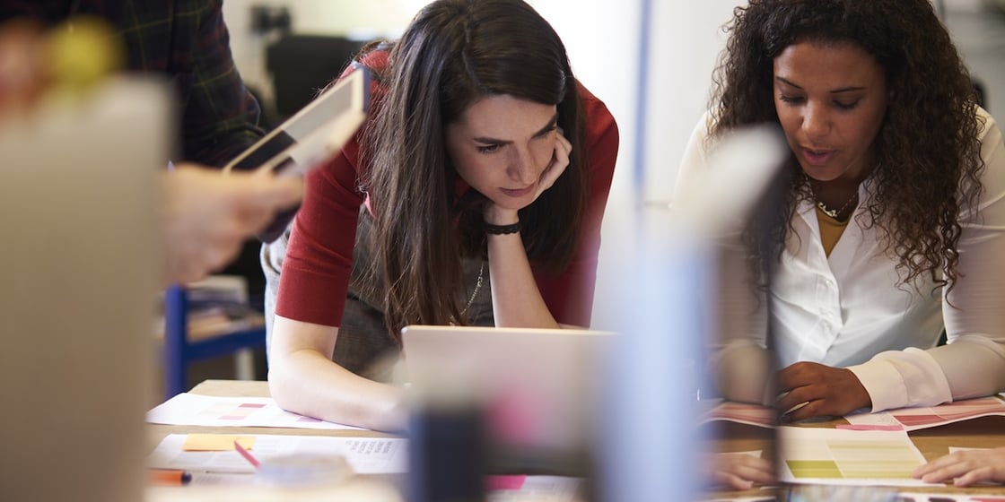 Two office workers reviewing documents and working on a laptop.