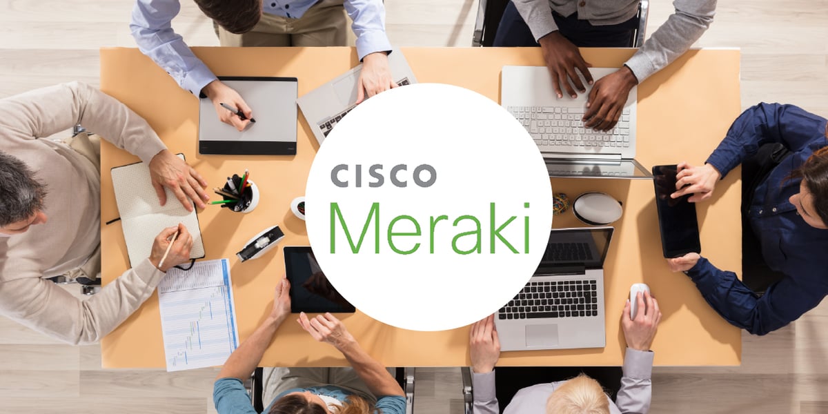 Photo of coworkers working around a conference table. The Cisco Meraki logo is inset atop a white circle.