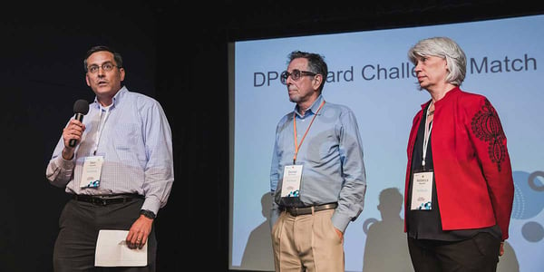 TechSoup's Ken Tsunoda, Daniel Ben-Horin, and Rebecca Masisak announce the DPO Challenge Match before an audience at the 2019 TechSoup Global Network Summit.